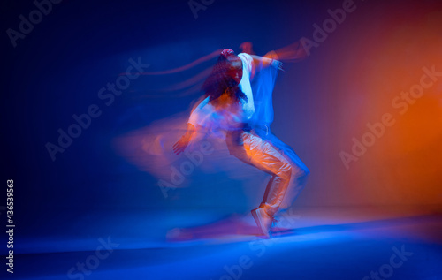 Dancing girl standing on toes in colourful neon studio light. Expressive contemporary hip hop dance. Long exposure