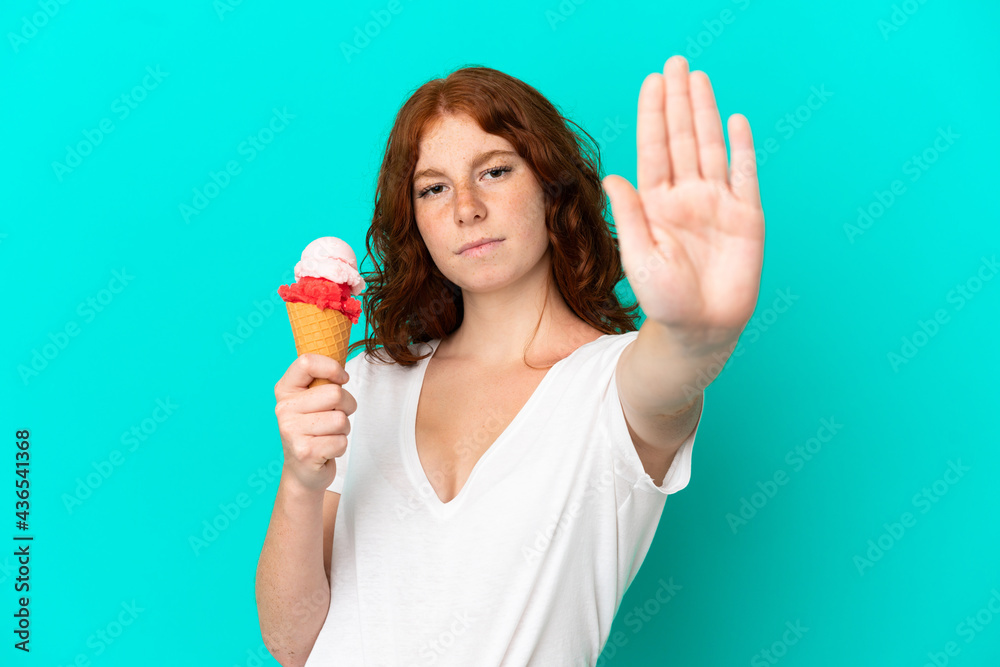 Teenager reddish woman with a cornet ice cream isolated on blue background making stop gesture Teenager reddish woman with a cornet ice cream isolated on blue background making stop gesture