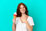 Teenager reddish woman with a cornet ice cream isolated on blue background giving a thumbs up gesture
