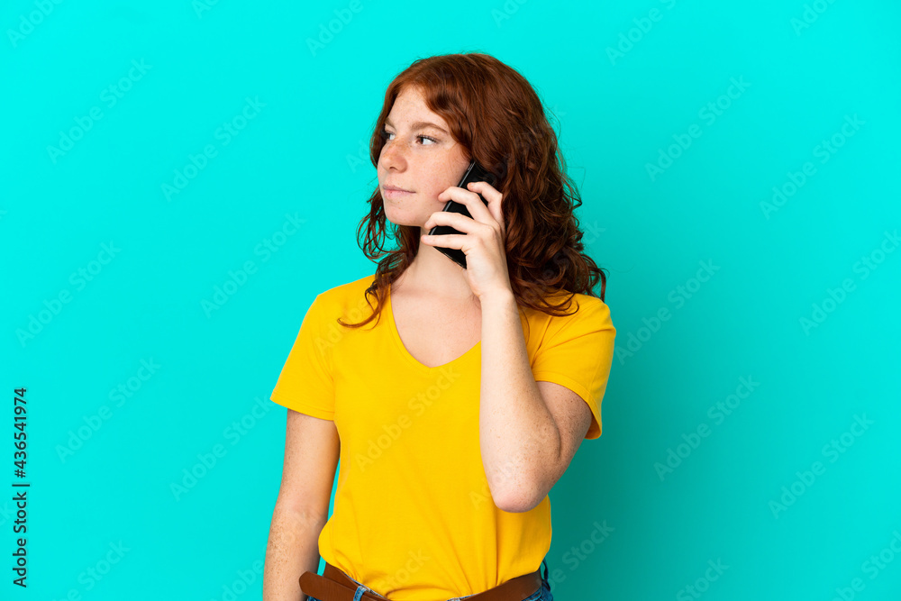 Teenager reddish woman using mobile phone isolated on blue background looking to the side Teenager reddish woman using mobile phone isolated on blue background looking to the side