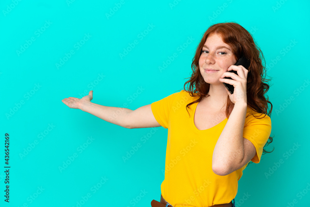 Teenager reddish woman using mobile phone isolated on blue background extending hands to the side for inviting to come Teenager reddish woman using mobile phone isolated on blue background extending hands to the side for inviting to come