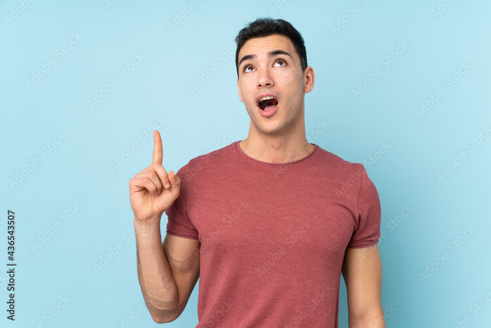 Young caucasian handsome man isolated on blue background pointing up and surprised Young caucasian handsome man isolated on blue background pointing up and surprised