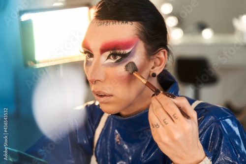Obraz na płótnie Drag queen with bright makeup applying highlighter at his face