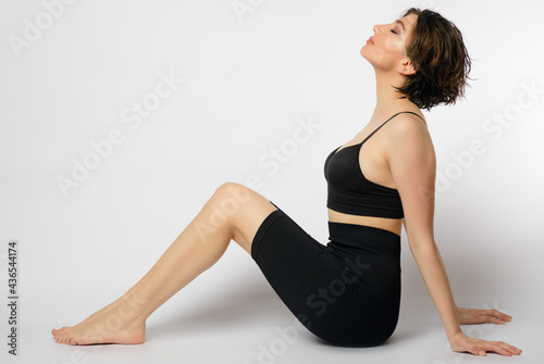 Woman on a white background sitting with a bra and spandex.
