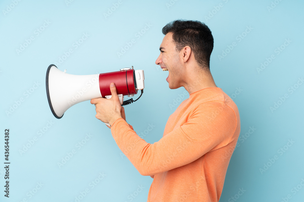 Young caucasian handsome man isolated on blue background shouting through a megaphone Young caucasian handsome man isolated on blue background shouting through a megaphone