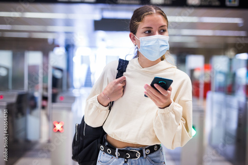 Confident girl in a protective mask with a mobile phone in her hands entered the subway during the pandemic, passing through the turnstile