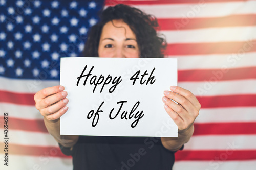 Young woman with the United States flag in the background holding a happy 4th of July sign