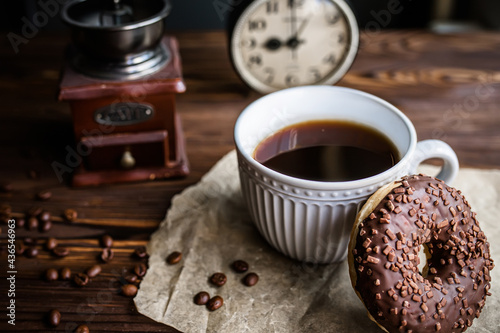 glass of coffee on table with clock in morning. vintage alarm clock showing 9am on the table next to a cup of coffee and a doughnut. Breakfast. Time management concept photo