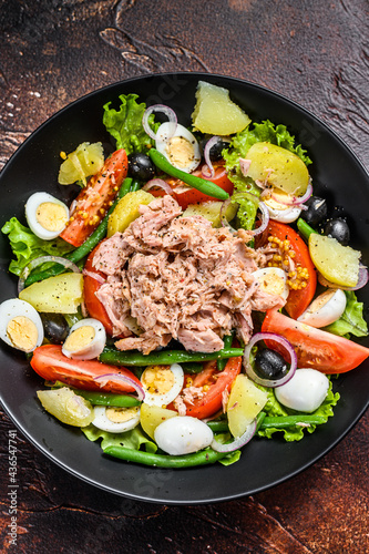 Healthy hearty salad with tuna, green beans, tomatoes, eggs, potatoes and black olives in a plate. Dark background. top view