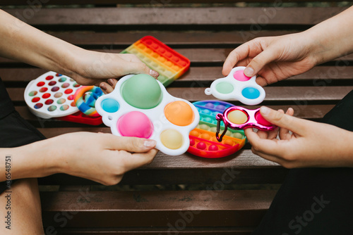 colorful trendy antistress sensory toy fidget push pop it and simple dimple in kid's hands, children share toys on the playground