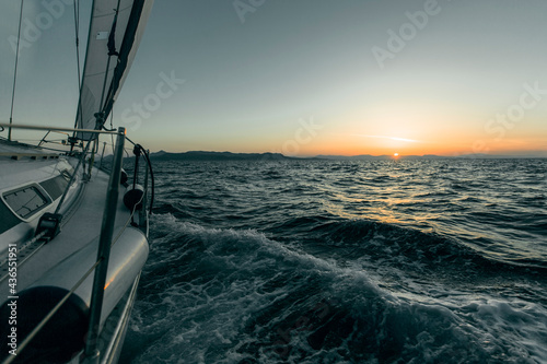 A sailing yacht glides through the waves at sea during sunset.