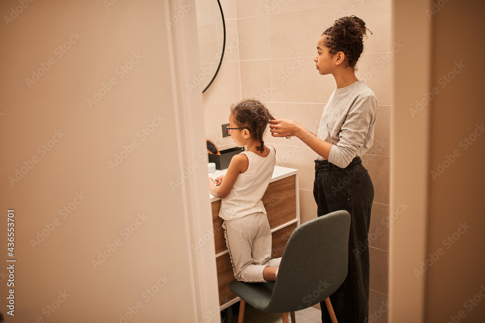 Girl helping to preparing hairstyle for her little sister while spending time at the bathroom Girl helping to preparing hairstyle for her little sister while spending time at the bathroom
