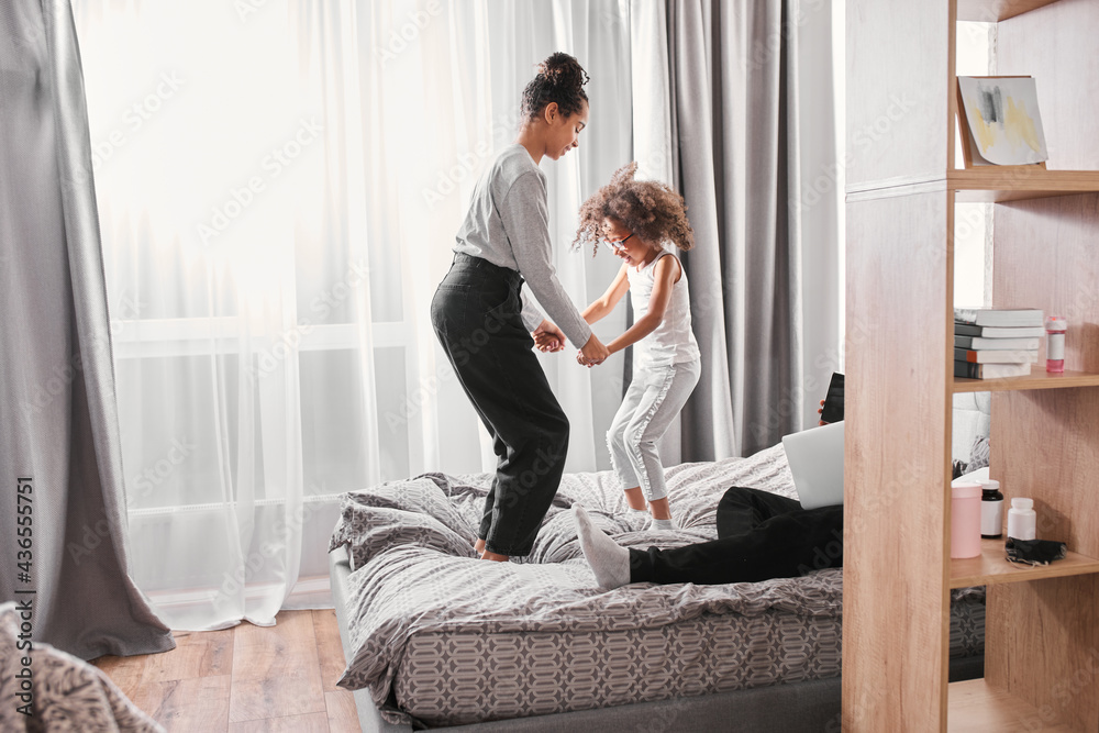 Sisters laughing and joking with each other while jumping at the bedroom Sisters laughing and joking with each other while jumping at the bedroom