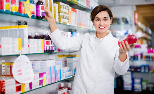 Young friendly smiling female pharmacist suggesting useful body care products in pharmacy