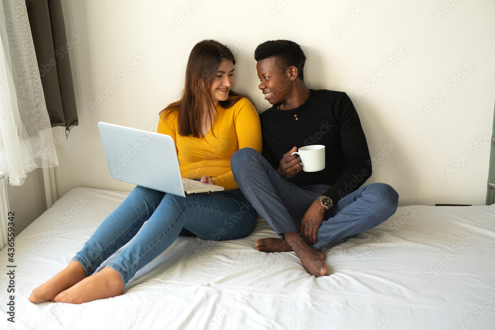 beautiful young couple african man and caucasian woman sit on bed with laptop beautiful young couple african man and caucasian woman sit on bed with laptop