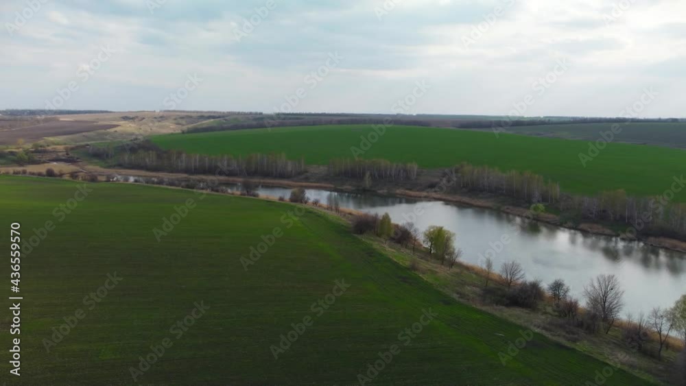Aerial cloudy agricultural view, flying above young green spring fields and lake. Rural scene with nice cloudscape and water Aerial cloudy agricultural view, flying above young green spring fields and lake. Rural scene with nice cloudscape and water