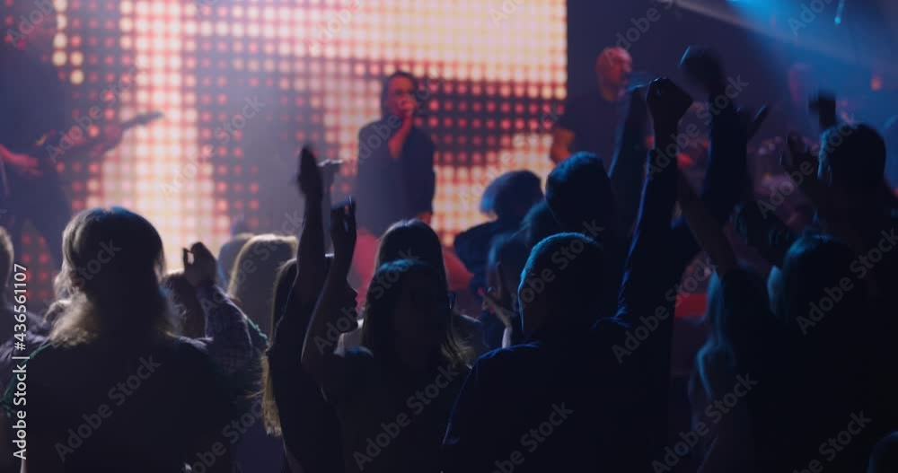 Crowd of people moving rhythmically into the groove with their arms raised. Music band are performing on the stage. Slow motion Crowd of people moving rhythmically into the groove with their arms raised. Music band are performing on the stage. Slow motion
