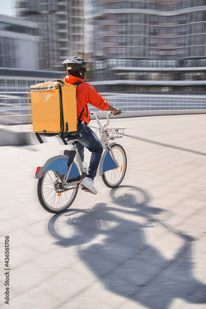 Obraz premium Courier with yellow backpack driving bike and coming to the client with parsels