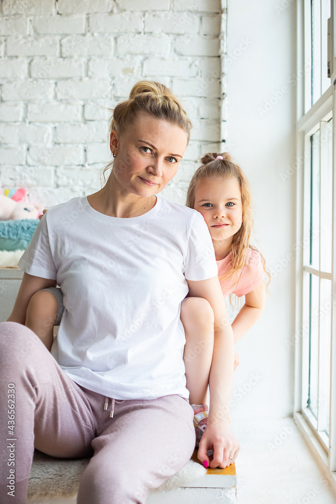 Little caucasian girl sitting together with mother on sitting on the windowsill Little caucasian girl sitting together with mother on sitting on the windowsill
