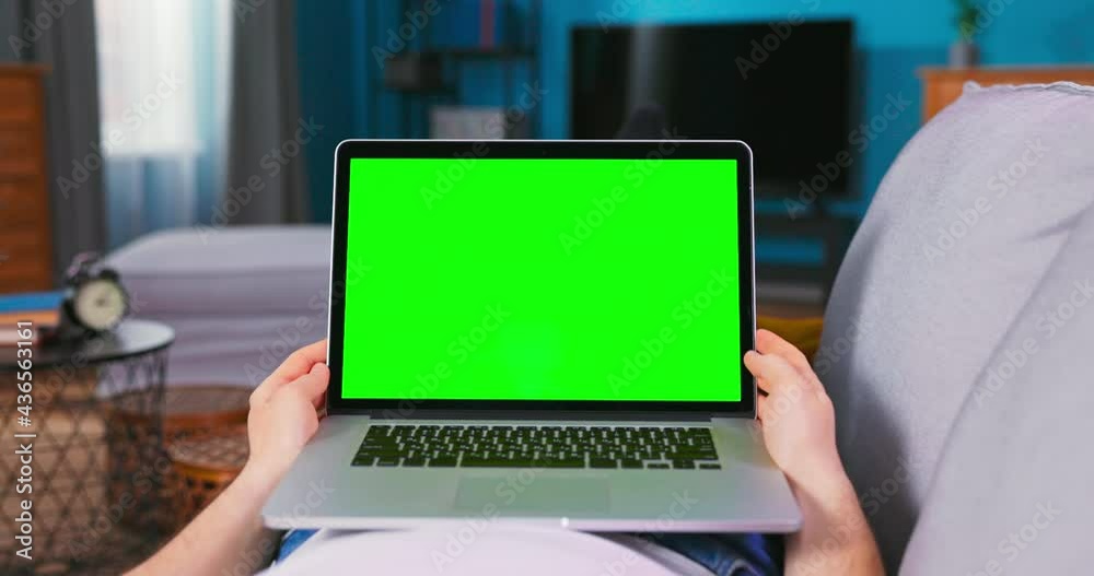 Green Mock-up Screen Laptop. Man is talking on video chat with friends, doctor or financial agent while is lying On a Couch in His Cozy Living Room. Point of View Camera Shot. Green Mock-up Screen Laptop. Man is talking on video chat with friends, doctor or financial agent while is lying On a Couch in His Cozy Living Room. Point of View Camera Shot.