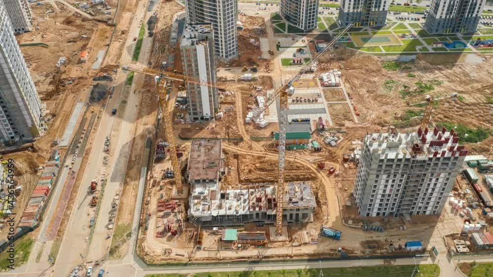 Aerial time-lapse hyperlapse tower cranes working on construction site in city. Drone shot constructions development on sunny day. Machinery and workers employed. Builders work on residential building