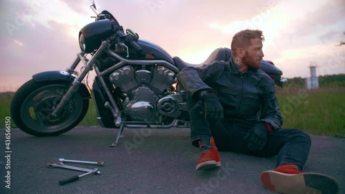 The biker's motorcycle broke down, he sits and waits for help