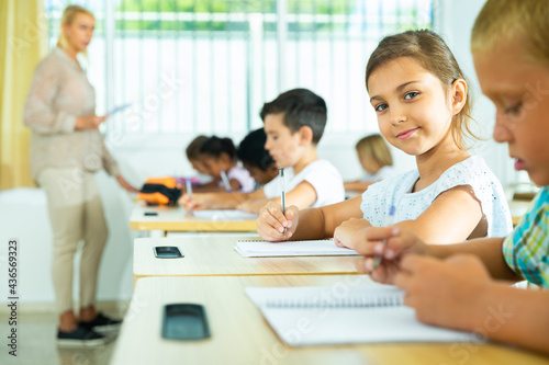 Portrait of positive tween schoolgirl sitting on lesson in classroom  looking at camera with smile
