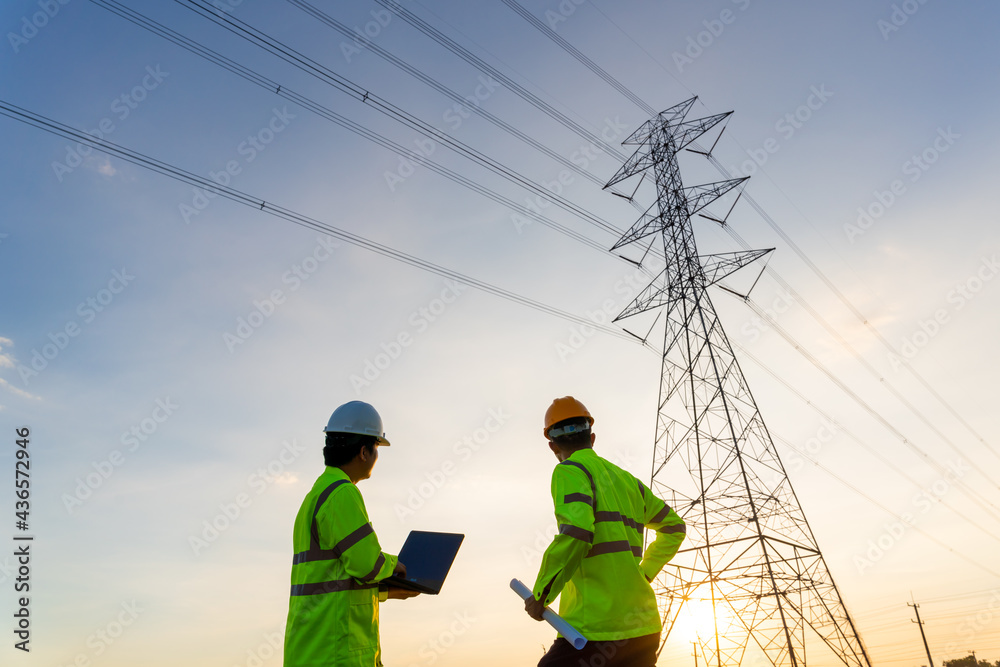 Team work of Engineers and Technician working inspections at the electric power station to view the planning work by producing electricity high voltage electric transmission tower at sunset Team work of Engineers and Technician working inspections at the electric power station to view the planning work by producing electricity high voltage electric transmission tower at sunset