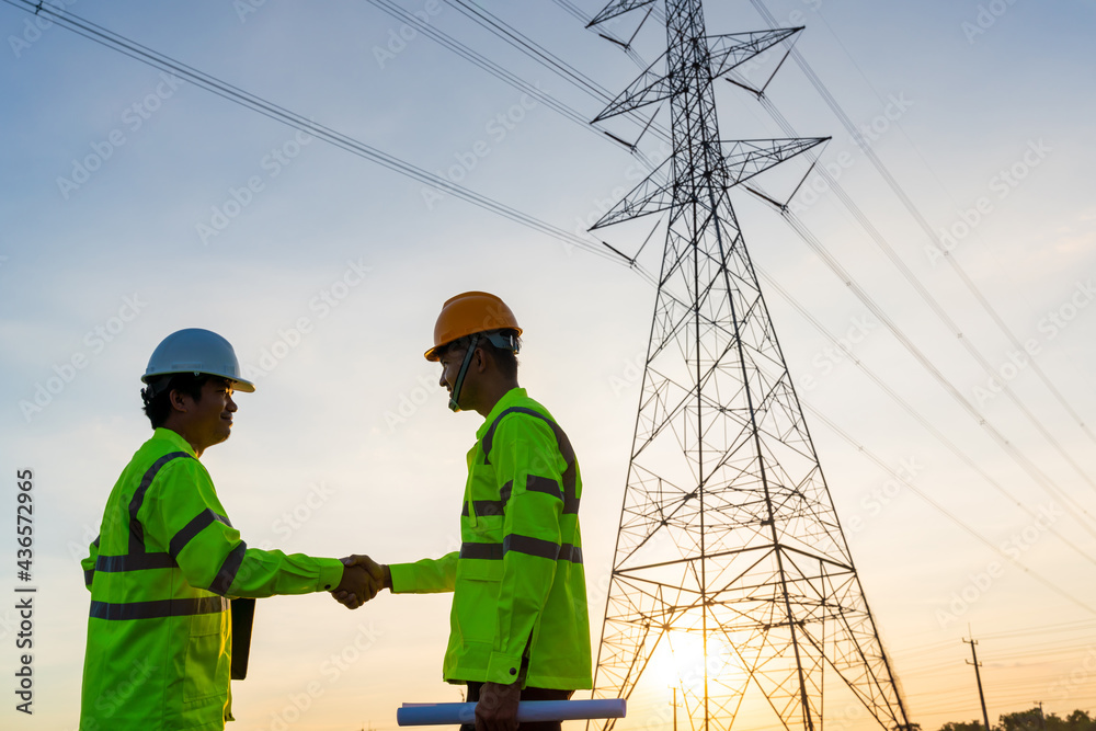 Team work of Engineers and Technician handshake after work inspections at the electric power station to view the planning work by producing electricity high voltage electric transmission tower Team work of Engineers and Technician handshake after work inspections at the electric power station to view the planning work by producing electricity high voltage electric transmission tower