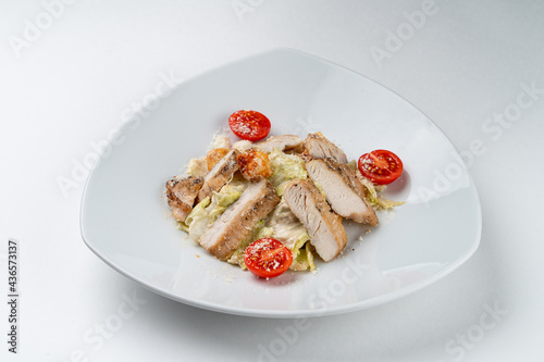 Classic caesar salad with crunchy lettuce and a whole grilled chicken breast, isolated on white background in a studio