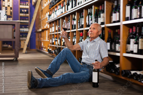 Man tasting red wine before buying sitting on floor in wine store