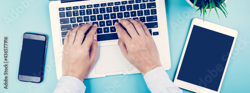 Hand of businessman working on laptop computer with plant and tablet and phone on desk in office, hand typing keyboard on notebook and workplace with copy space, top view, flat lay, business concept.