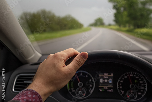 Close-up of male hand holding steering wheel, driving the car. Background of blurred road in rainy day. Transportation concept.