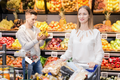 Portrait of happy positive smiling woman satisfied with purchases in shopping cart at fruit store