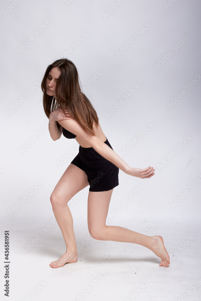 Young slim athletic girl, with long hair, in a black top and shorts, dancing in the white studio
