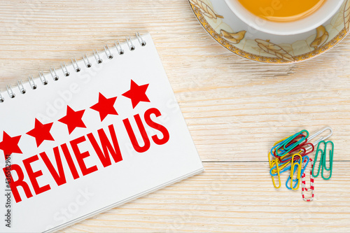 review us 5 stars, customer opinion concept, notepad on white aged wooden table with tea cup and paper clips