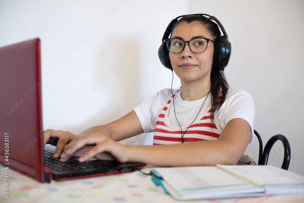 Woman wearing headphones, using laptop, using cell phone, writing notes and smiling, online class concept Woman wearing headphones, using laptop, using cell phone, writing notes and smiling, online class concept
