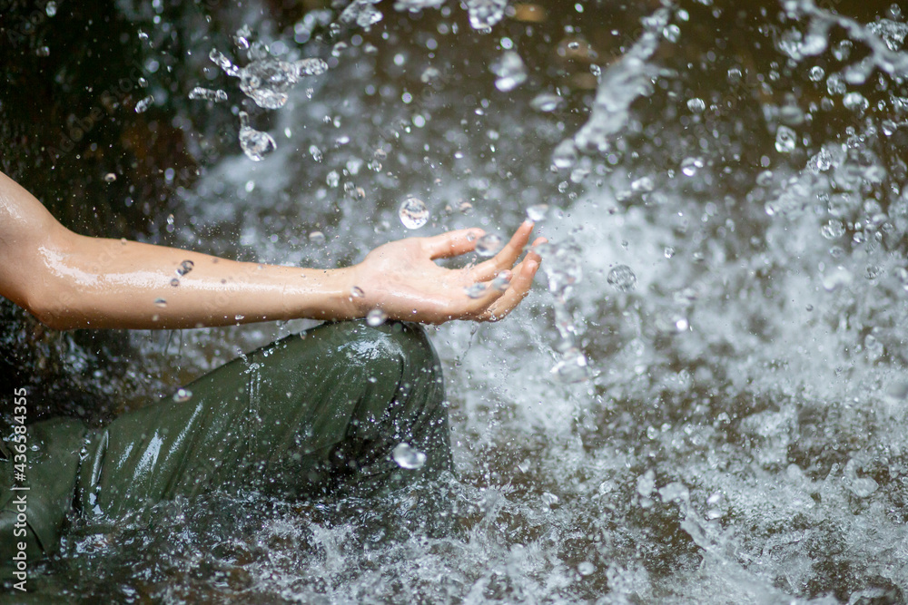 selective focus, a man's hand, supports the water beside the waterfall Gives a refreshing feeling of moisture And natural sensations, waterfalls and small streams in Thailand in the summer,