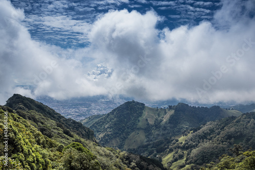 Line of mountains with grass and trees surrounding the capital of Costa Rica on a sunny day full of white clouds