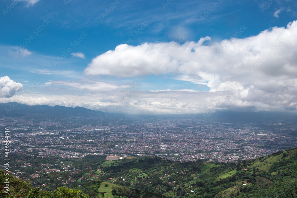 panoramic view of the green and tree-filled mountains surrounding the capital of San Jose, Costa Rica on a sunny morning with white clouds