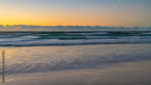 Clear skies sunrise seascape with waves and a low cloud bank on the horizon