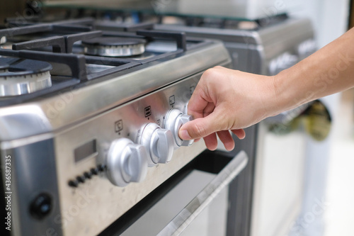 Male hand turning temperature knob of modern oven in kitchen showroom. Buying cooking appliance for domestic kitchen. Home improvement concept