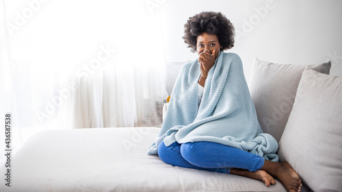 Foto Sick young african woman feeling cold covered with blanket sit on sofa, ill blac