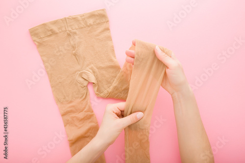 Cuadro en lienzo Young adult woman hand stretching brown nylon pantyhose on light pink table background