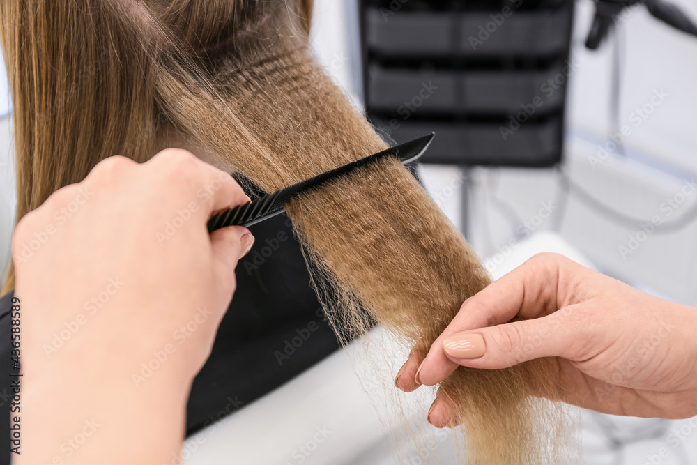 Naklejka premium Female hairdresser curling hair of client in beauty salon, closeup