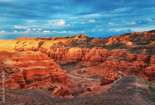 The view from the top to the canyon, sunset sky, erosion, plateau, cloudy sky and mountains on the horizon. Red rocks and layers. Panorama of the Charyn canyon in Kazakhstan.