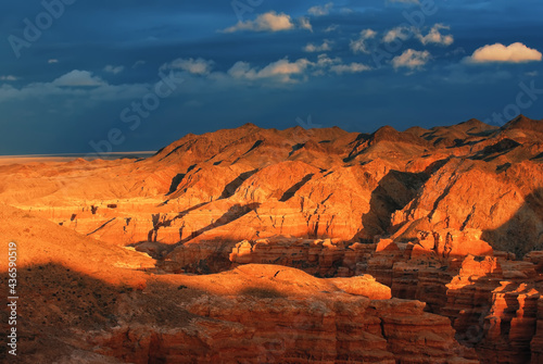 Sunset in the canyon, sunrays on the mountains, erosion, plateau, cloudy sky and mountains on the horizon. Red rocks and layers. Charyn canyon in Kazakhstan