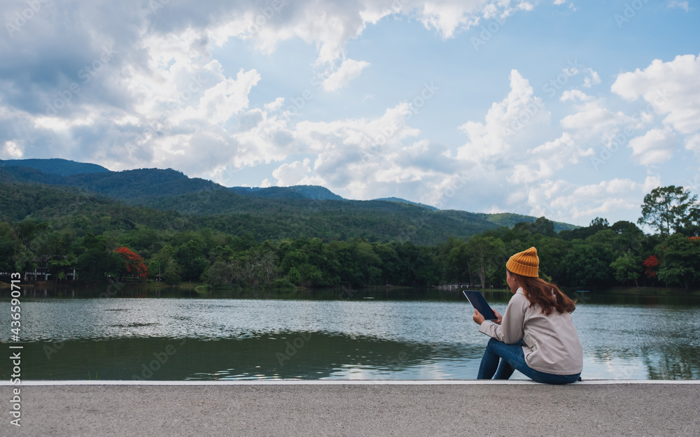A young woman holding and using digital tablet while traveling mountains and lake