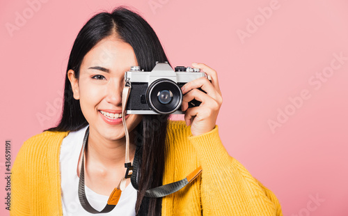 .Attractive energetic happy Asian portrait beautiful young woman smiling photographer taking a picture and looking viewfinder on retro vintage photo camera ready to shoot isolated on pink background