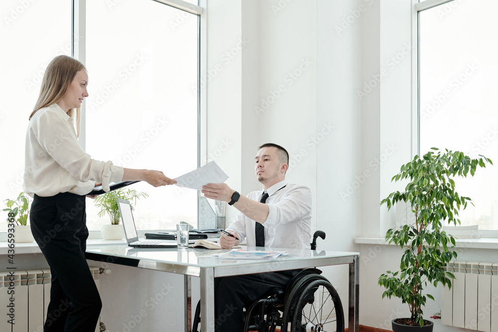 Director in wheelchair passing signed document to his secretary over table Director in wheelchair passing signed document to his secretary over table